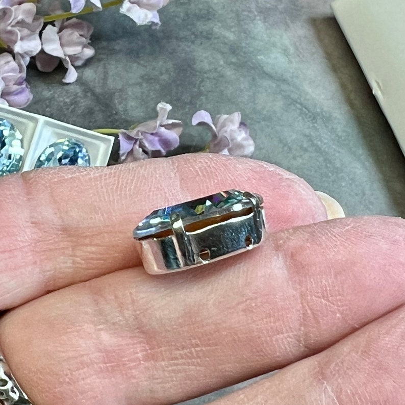 May include: A clear, faceted, iridescent gemstone set in a silver bezel setting. The gemstone is oval shaped and has a rainbow of colors.