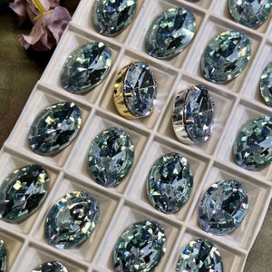 May include: A tray of oval-shaped, light blue rhinestones with a gold and silver setting. The rhinestones are arranged in a grid pattern.