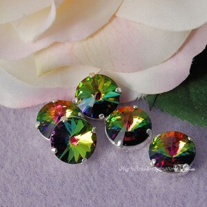 May include: Five iridescent round rhinestones with silver settings. The rhinestones display a spectrum of colors, including green, yellow, orange, and purple. The background features a soft pink and white flower and a light purple surface.