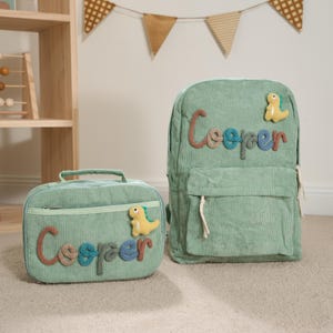 Puede incluir: Un juego a juego de mochila y bolsa de almuerzo de pana verde menta. El nombre "Cooper" est&aacute; cosido en cada art&iacute;culo con hilo colorido. Cada bolsa tiene una aplicaci&oacute;n de dinosaurio amarillo.