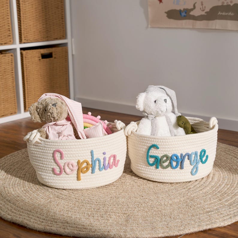 May include: Two white rope storage baskets with colorful embroidered names, "Sophia" and "George", filled with stuffed animals and toys.