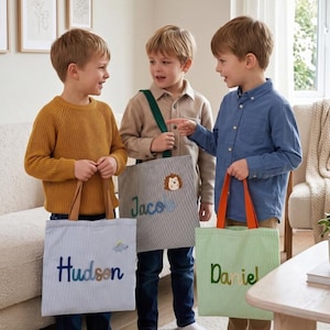Peut inclure: Trois sacs fourre-tout rectangulaires en tissu avec des prénoms personnalisés brodés sur le devant. Un sac est bleu clair avec le nom Hudson, un est gris avec le nom Jacob et un écusson hérisson, et un est vert clair avec le nom Daniel.