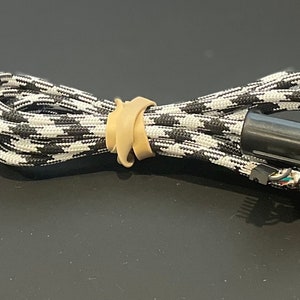 May include: A black and white braided cable with a rubber band holding it together. The cable has a black connector with a small metal pin on the end.