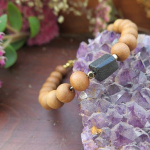 May include: A wooden beaded bracelet with a black stone bead. The bracelet is resting on a bed of amethyst crystals.