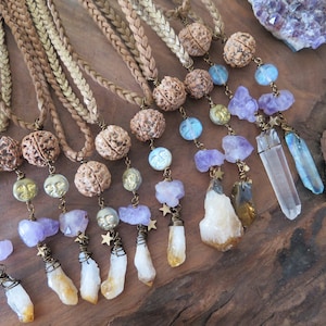 May include: A collection of handmade necklaces featuring a variety of crystals, including amethyst, citrine, and clear quartz. Each necklace has a brown braided cord and a small, round bead.