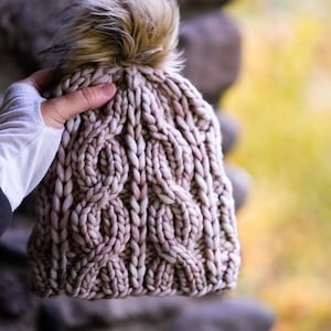 May include: A pink and white cable knit beanie with a fluffy brown pom pom.