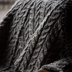 May include: A close-up of a gray knitted blanket with a cable knit pattern.