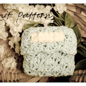 May include: A light blue knitted pouch with a white label that says "Knit Pattern" in a wicker basket with white flowers.