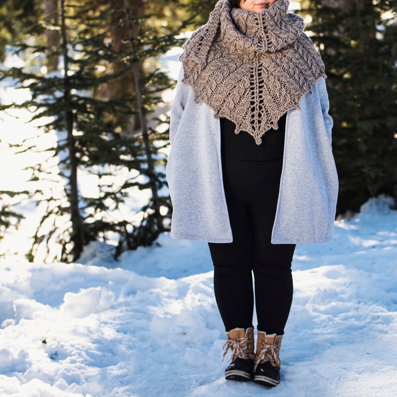 May include: A woman wearing a gray coat and black leggings with a brown crocheted shawl. She is standing in a snowy landscape.