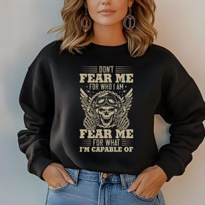 Op de afbeelding: Zwart sweatshirt met een grafische print van een schedel met een bril en pistolen. De tekst luidt "Don't Fear Me For Who I Am Fear Me For What I'm Capable Of."