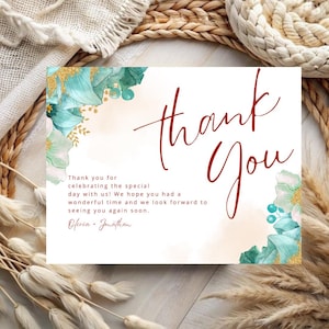 May include: Thank you card with a watercolor floral design in shades of teal and gold. The text "Thank You" is written in large, bold, red script. The card includes the text "Thank you for celebrating the special day with us! We hope you had a wonderful time and we look forward to seeing you again soon. Olivia & Jonathan."