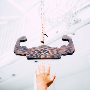 May include: A wooden sign shaped like a bicep hangs from a chain. The sign is dark brown with a wood grain pattern. The sign has a triangular logo in the center.