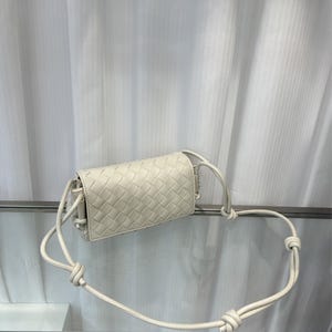 Op de afbeelding: Off-white, geweven leren crossbodytas. De rechthoekige tas heeft een herhalend vierkant patroon en een lange, geknoopte riem. De tas is gemaakt van zacht, soepel leer en heeft een minimalistisch ontwerp.