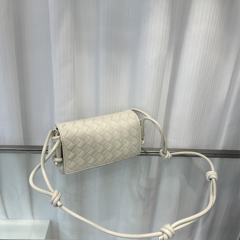 Op de afbeelding: Off-white, geweven leren crossbodytas. De rechthoekige tas heeft een herhalend vierkant patroon en een lange, geknoopte riem. De tas is gemaakt van zacht, soepel leer en heeft een minimalistisch ontwerp.