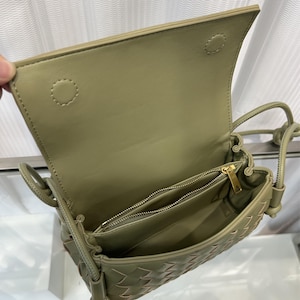Op de afbeelding: Olijfgroene crossbodytas met een geweven ontwerp. De tas heeft een klepsluiting en een goudkleurige ritssluiting. De binnenkant onthult meerdere compartimenten. De riem is verstelbaar.