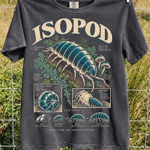 Puede incluir: Una camiseta gris carbón con un gráfico grande y detallado de un isópodo. El diseño incluye ilustraciones de estilo científico, etiquetas de texto como ISOPOD, LIFE CYCLE y pequeños diagramas que muestran el desarrollo del animal.