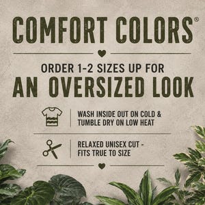 Puede incluir: Imagen con el texto "COMFORT COLORS" e instrucciones para pedir 1-2 tallas m&aacute;s grandes para un look oversize. El texto adicional incluye instrucciones de lavado y secado, y la frase "RELAXED UNISEX CUT - FITS TRUE TO SIZE". El fondo es de un color neutro y texturizado.