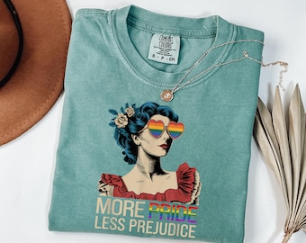 Könnte beinhalten: Ein blaugrünes T-Shirt mit einer Vintage-Illustration einer Frau, die eine Regenbogen-Herz-Sonnenbrille trägt. Der Text "More Pride Less Prejudice" ist unter der Illustration gedruckt.