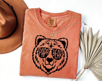 May include: A coral-colored t-shirt with a black bear graphic wearing sunglasses and the text "Papa Bear".