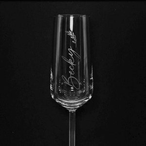 May include: A clear glass champagne flute with the name "Becky" etched on the side. The flute has a delicate stem and a wide base.