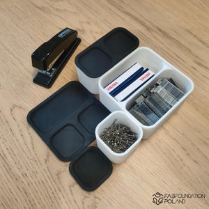 Pu&ograve; includere: Un assortimento di forniture per ufficio, tra cui una pinzatrice nera, contenitori bianchi e neri e un vassoio nero. I contenitori contengono punti metallici, spilli e scatole con l'etichetta "SIGMA". La pinzatrice ha il testo "OFFICE WORK" stampato.