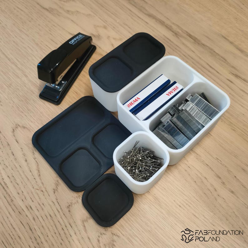 Pu&ograve; includere: Un assortimento di forniture per ufficio, tra cui una pinzatrice nera, contenitori bianchi e neri e un vassoio nero. I contenitori contengono punti metallici, spilli e scatole con l'etichetta "SIGMA". La pinzatrice ha il testo "OFFICE WORK" stampato.