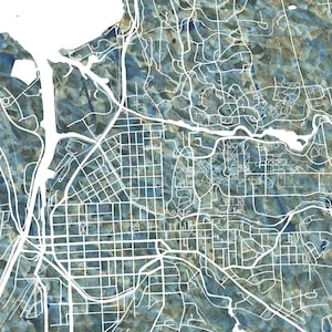 Puede incluir: Un mapa de acuarela de Ithaca, Nueva York, con un esquema de color azul y verde. El mapa muestra las calles y vías fluviales de la ciudad. La palabra "ITHACA" está impresa en blanco debajo del mapa.