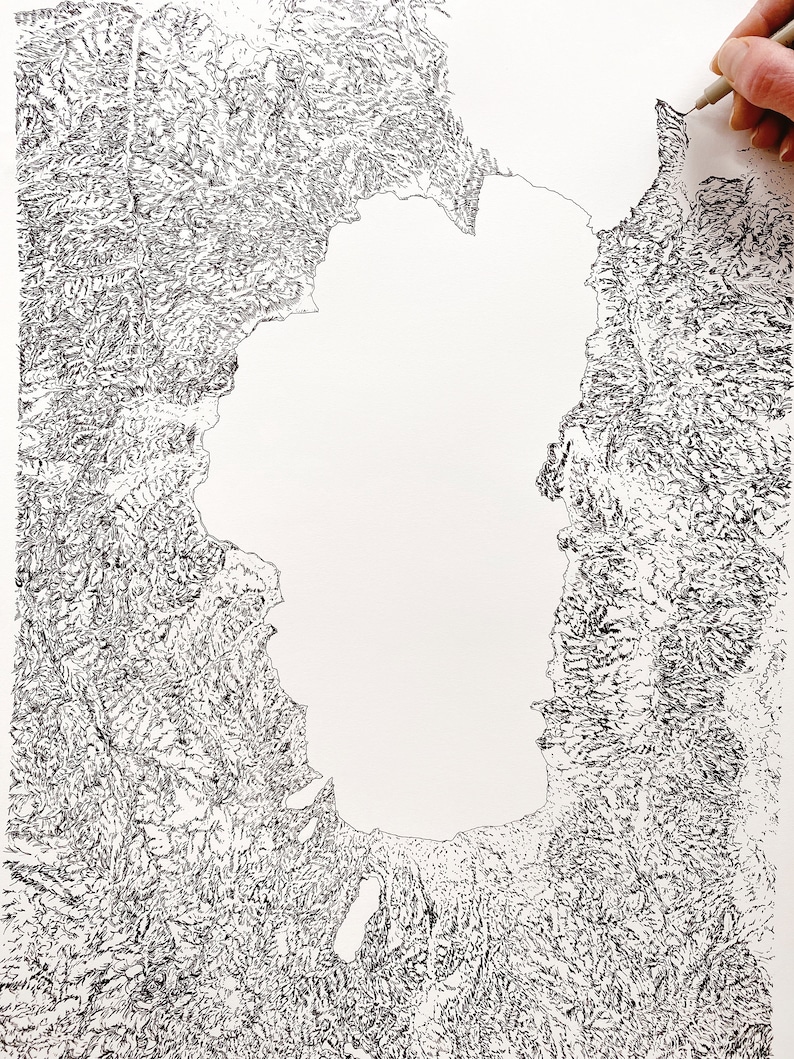 Op de afbeelding: Gedetailleerde zwart-wit topografische kaartillustratie. De kaart toont een groot waterlichaam omgeven door getextureerd land, met fijne lijnen die diepte en hoogte cre&euml;ren. Een hand tekent met een pen op de kaart.