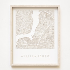 以下が含まれることがあります： ウィリアムズバーグ、ニューヨークのベージュの水彩画の地図の額装プリント。地図には、街の通りの様子と水路が描かれています。プリントは明るい木製の額縁に入っています。