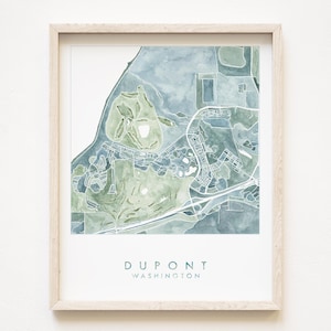 May include: Watercolor map print of Dupont, Washington, in shades of blue and green. The artwork is framed in a light wood frame. The city name and state are printed in a teal font at the bottom of the print.