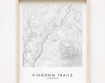 May include: A black and white topographic map print of the Kingdom Trails in Vermont. The print is framed in a light wood frame.