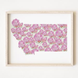May include: A framed print featuring the outline of Montana filled with pink floral illustrations. The flowers have detailed petals and are set against a light green background. The frame is a light wood color.