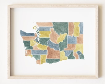 May include: Watercolor map of Washington State, framed in a light wood. The map is divided into counties, each colored in shades of blue, green, yellow, and brown. The artwork is displayed on a white background.