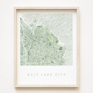 Könnte beinhalten: Ein gerahmter Druck einer grün-weißen Karte von Salt Lake City, Utah. Die Karte ist in einem hellen Holzrahmen und der Name der Stadt ist unter der Karte gedruckt.