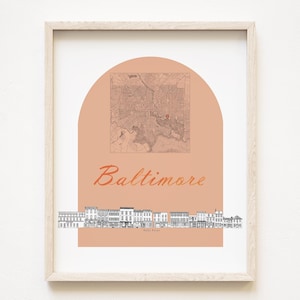 May include: Framed art print showing a map of Baltimore within a peach-coloured arch, with the city's name in cursive. A black and white line drawing of a street scene is below. The print is in a light wood frame.