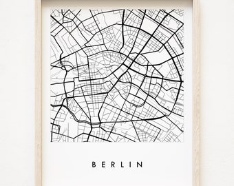 Puede incluir: Un mapa de Berlín, Alemania, en blanco y negro, impreso en papel blanco y enmarcado en un marco de madera claro. La palabra "BERLIN" está impresa en negro debajo del mapa.