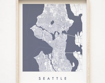 May include: A framed print of a map of Seattle, Washington. The map is in a light gray color with white lines showing the streets and waterways. The background is a dark gray color. The word "SEATTLE" is printed in white at the bottom of the map.