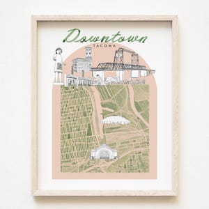 May include: A framed art print featuring a map of Tacoma, Washington, with illustrations of landmarks and the text "Downtown Tacoma." The artwork includes a pink arch and is in a light wood frame.
