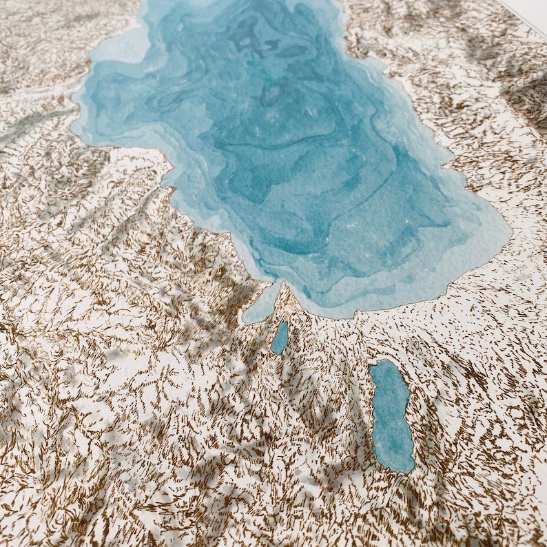 Op de afbeelding: Een gedetailleerde, artistieke kaart met een lichtblauwe meer omgeven door getextureerd, gebroken wit land met bruine contourlijnen. De kaart heeft een driedimensionaal effect.
