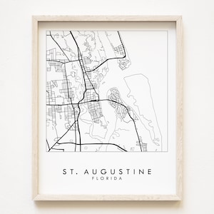 May include: Black and white line art print of a map of St. Augustine, Florida. The print is framed in a light wood frame.