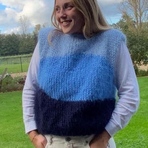 Op de afbeelding: Een blauwe, witte en donkerblauwe gestreepte gebreide vest met een pluche textuur. De vest is mouwloos en heeft een ronde hals.