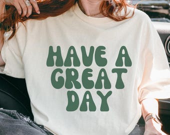 May include: Cream-coloured sweatshirt featuring the text "HAVE A GREAT DAY" in large, retro-style, dark green lettering. The sweatshirt has a relaxed fit and long sleeves, suitable for casual wear.