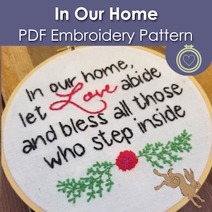 May include: A PDF embroidery pattern in a wooden hoop. The white fabric features the words "In our home, let love abide and bless all those who step inside" in black and red thread. Green and red floral embroidery accents the text.