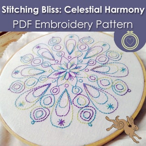 May include: A white embroidery hoop with a colorful mandala design stitched in purple, blue, and green thread. The design features a central flower with swirling patterns radiating outwards. The hoop is on a wooden surface.