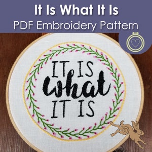 May include: Embroidered hoop art with a floral wreath and the text "It is what it is".