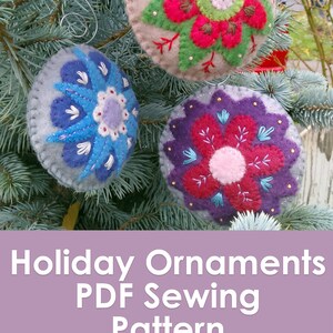 May include: Three felt Christmas ornaments with embroidered flower designs. The ornaments are red, blue, and purple with white and green accents. The ornaments are hanging on a green pine tree branch. Holiday Ornaments PDF Sewing Pattern Muse of the Morning.com