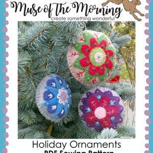 May include: Three felt ornaments with embroidered floral designs in shades of red, green, blue, and purple. The ornaments are hanging on a pine tree branch. The text "Holiday Ornaments PDF Sewing Pattern www.museofthemorning.com" is at the bottom of the image.
