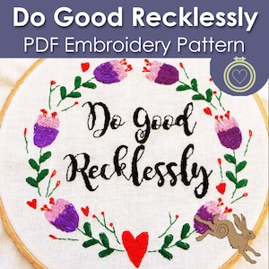 Op de afbeelding: Borduurwerk op een hoepel met een bloemenkrans en de tekst "Do Good Recklessly". De krans is gemaakt van paarse en roze bloemen met groene bladeren en rode bessen. Een rood hart bevindt zich aan de onderkant van de hoepel.
