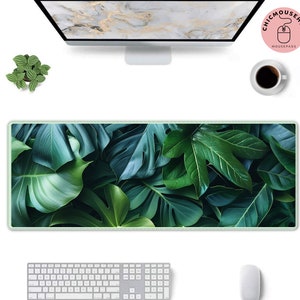 May include: A green tropical leaf patterned mouse mat with a white border. The mouse mat is on a white surface with a computer monitor, a keyboard, a mouse, and a potted plant.