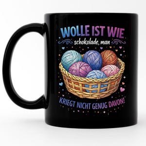 Könnte beinhalten: Schwarze Keramik-Tasse mit einem Korb voller bunter Wollknäuel. Die Tasse trägt den Text "Wolle ist wie Schokolade, man, kriegt nicht genug davon!" in einer Farbverlaufs-Schrift. Das Design beinhaltet Herzen und Sterne.